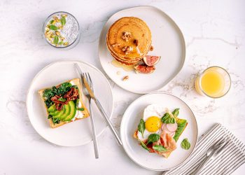A plate of grilled salmon, boiled eggs, fresh spinach and walnuts arranged on a light kitchen counter