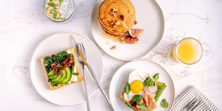 A plate of grilled salmon, boiled eggs, fresh spinach and walnuts arranged on a light kitchen counter