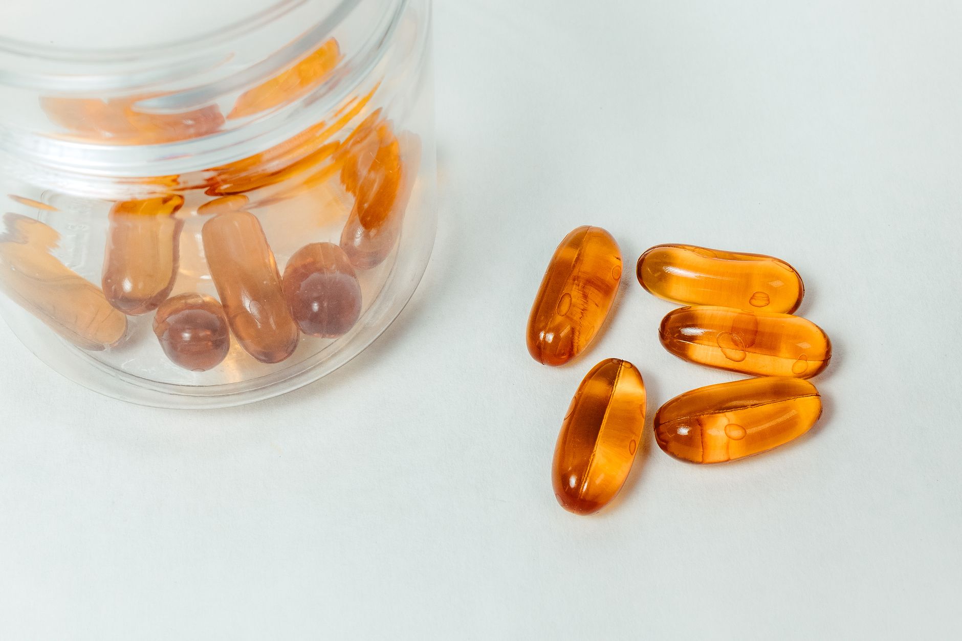 Capsules and softgel supplements spilling from an open bottle onto a wooden table beside a glass of water