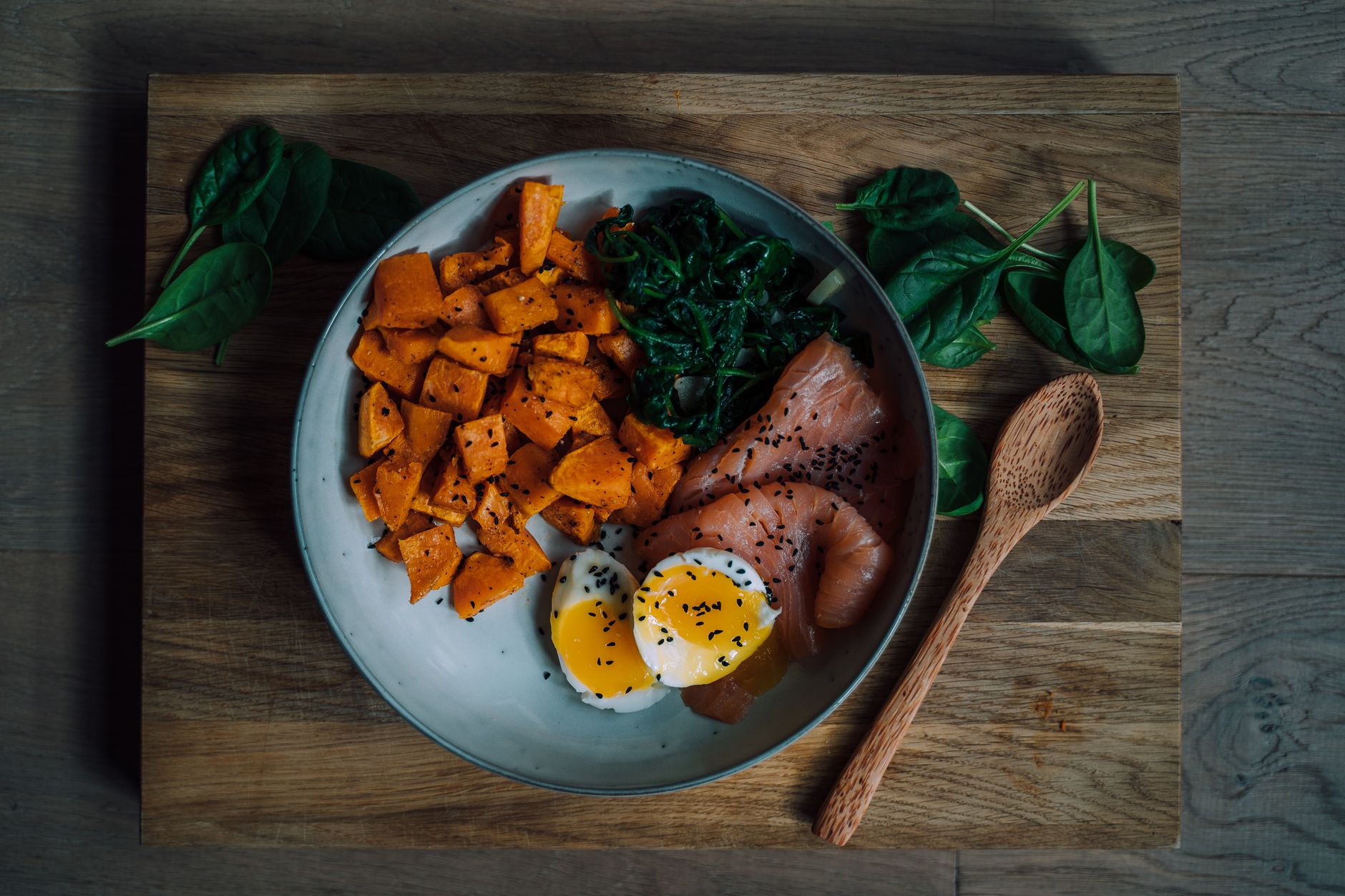 Salmon fillet, eggs, fresh spinach, walnuts and pumpkin seeds arranged on a light wooden counter.