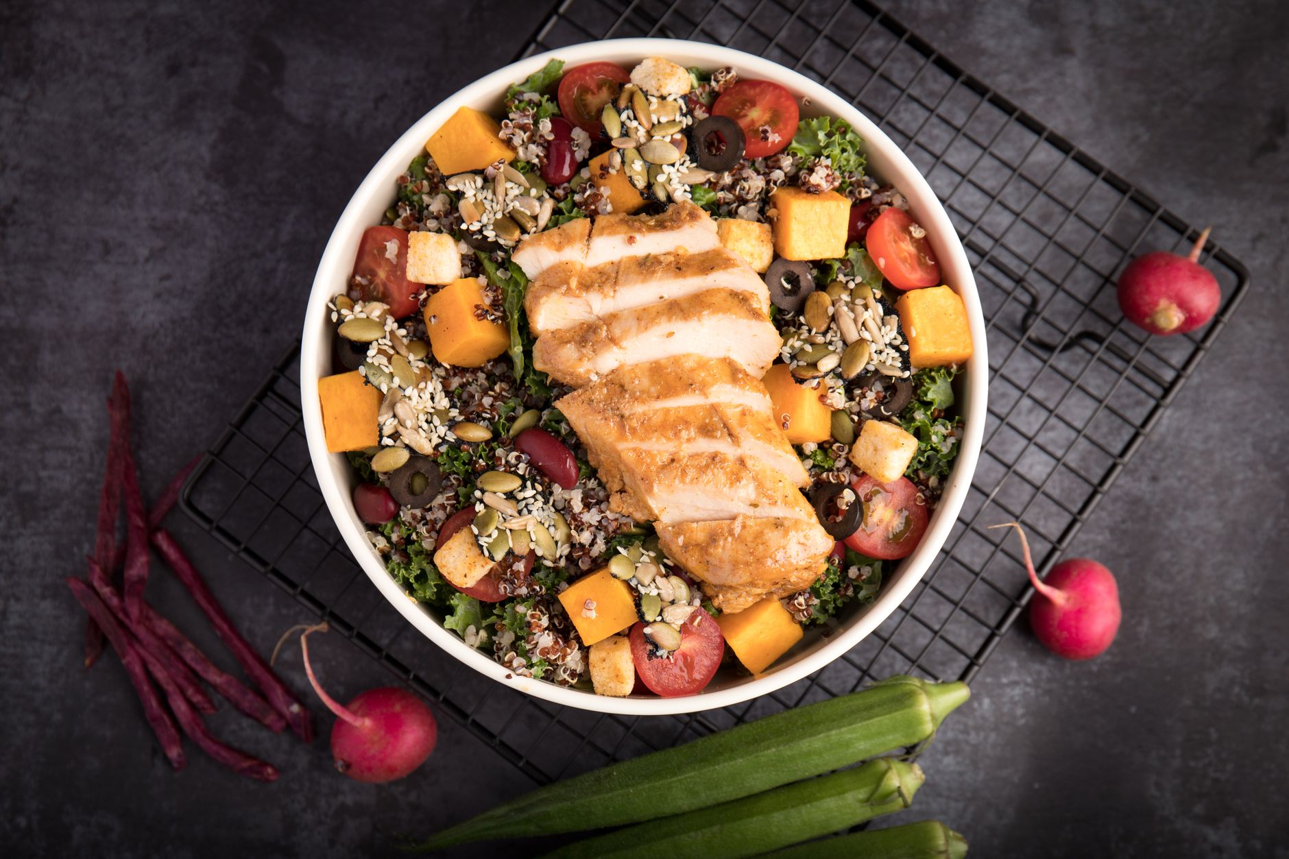 Protein bowl with sliced grilled chicken, quinoa, chickpeas and steamed broccoli on a kitchen table.