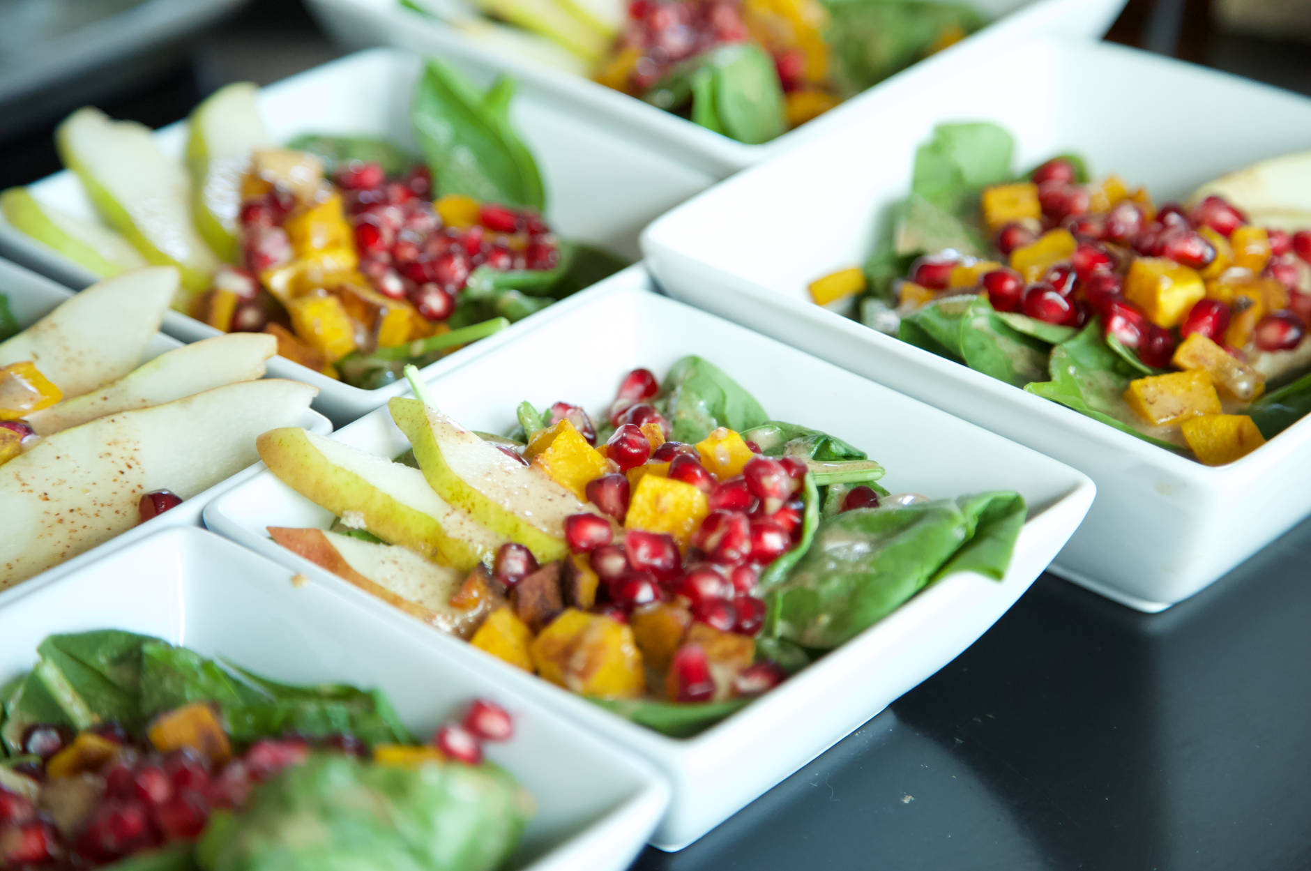 White bowl of spinach salad topped with orange slices, red bell pepper strips and pumpkin seeds.