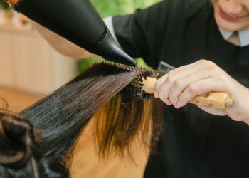 Woman gently brushing her long, shiny dark hair with a wide-tooth comb near a bright window