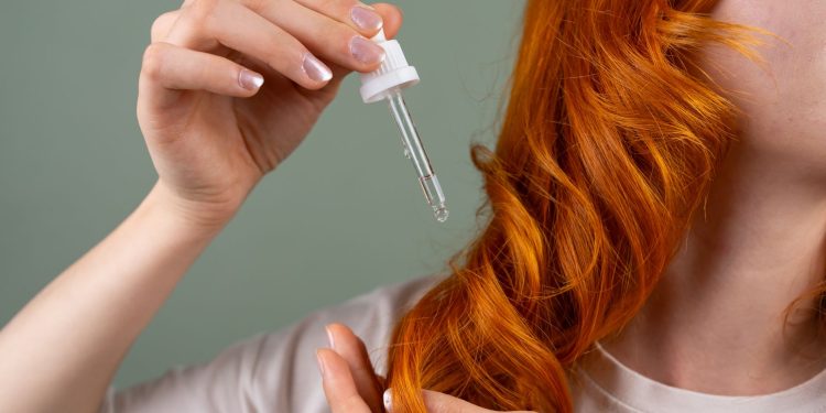 A woman standing in soft daylight, working coconut oil through the mid-lengths of her long dark hair with her fingers.