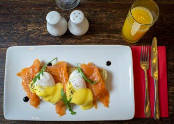 Boiled eggs, a salmon fillet, lentils, and almonds arranged on a wooden kitchen table