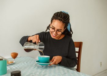 A woman in a bathroom pouring cloudy rice water from a glass jar over her long damp hair