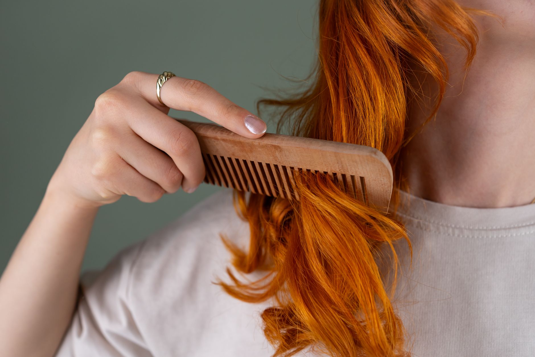 A woman gently combing through her wet curly hair with a wide-tooth comb near a mirror